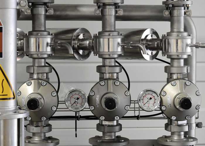 An array of silver, industrial-looking valves and gauges, suggesting a complex mechanical system.
