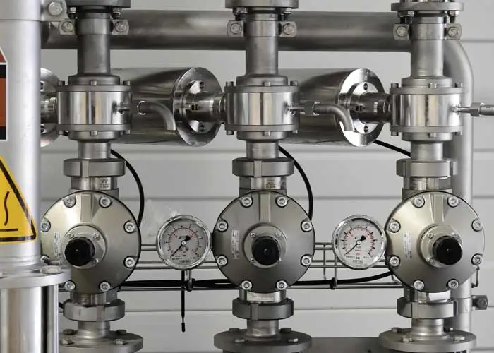 An array of silver, industrial-looking valves and gauges, suggesting a complex mechanical system.