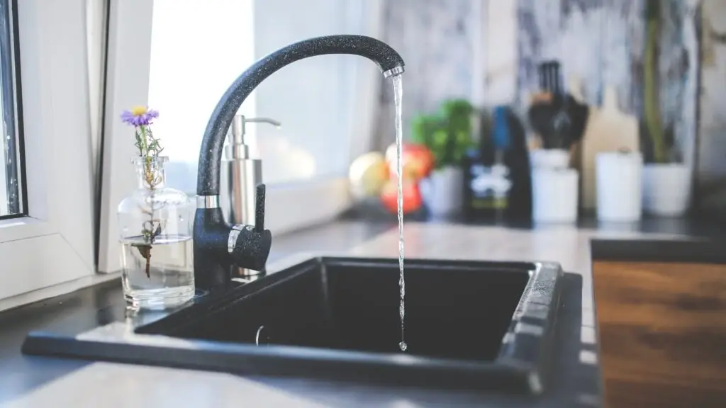 Image showing a black kitchen faucet with water flowing from the spout, surrounded by various household items on a kitchen counter