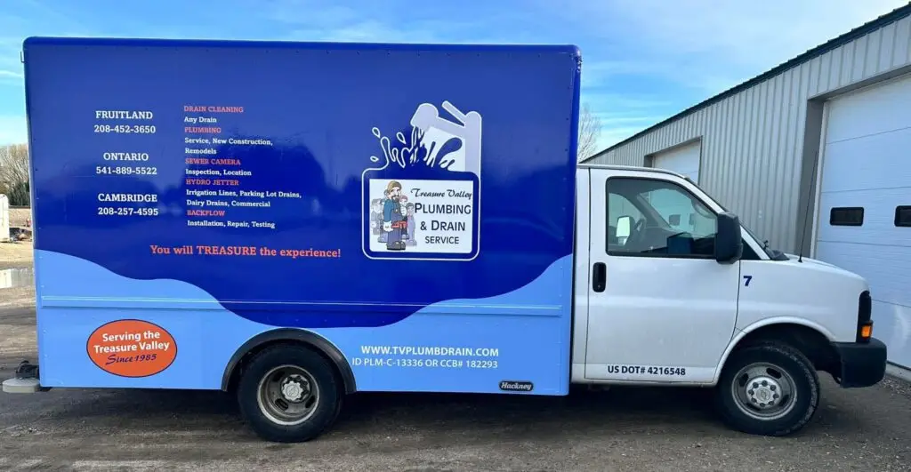 A close-up image of the side of a blue plumbing and drain service van, displaying the company's name, contact information, and services.