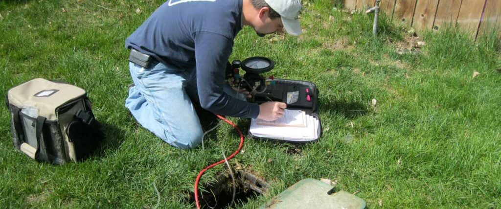 An image showing a worker using a power tool to perform some kind of landscaping or ground maintenance work, with a grassy area and fencing visible in the background.