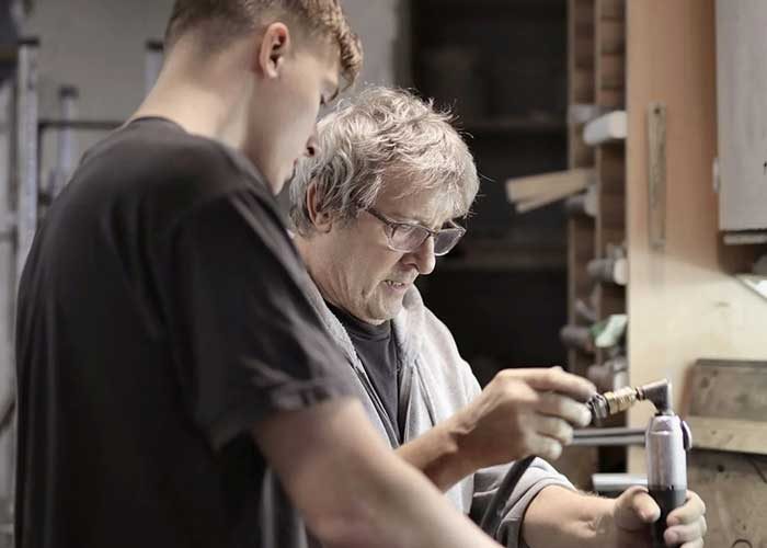 Two men, one older and one younger, working together on a woodworking project in a workshop setting